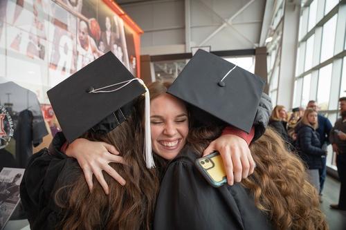 An individual hugs two graduating students at commencment